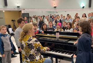 Chorleiterin am Klavier im Hintergrund der Chor